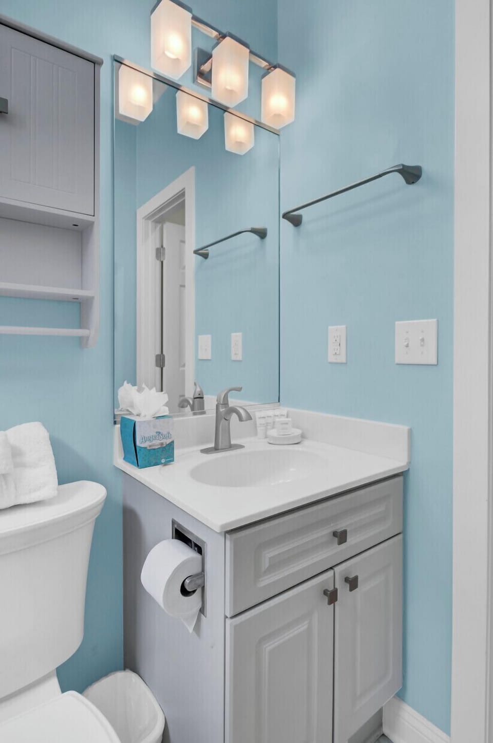 Refresh in your private bathroom with modern vanity, bright lighting, and calming blue walls.