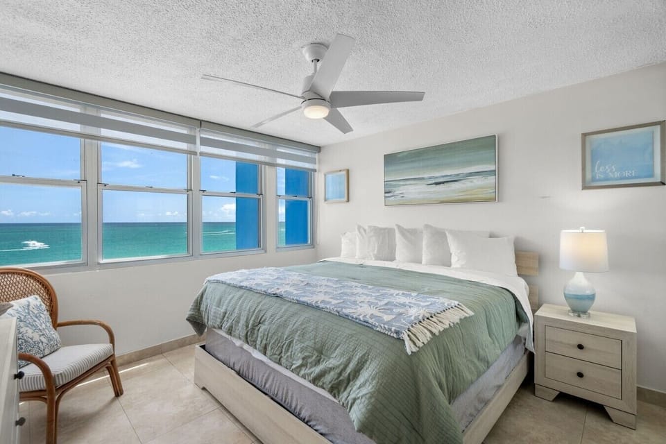 Ocean-view bedroom with king bed, coastal décor, Smart TV, and ceiling fan