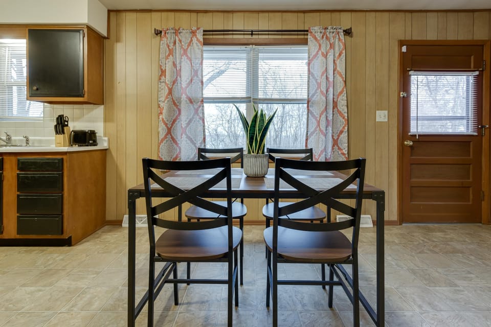 Dining area with black metal-framed table and chairs, snake plant centerpiece, and patterned curtains on window.