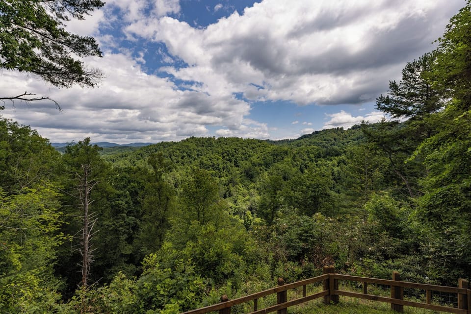 Sweeping mountain vistas surround the property, offering a peaceful retreat nestled among rolling forested hills beneath dramatic skies.
