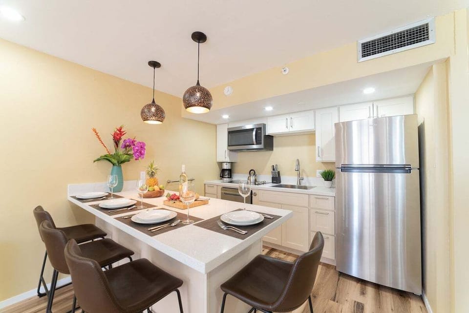 Dining table set for four beneath pendant lights, stainless fridge and modern kitchen ready for gatherings.