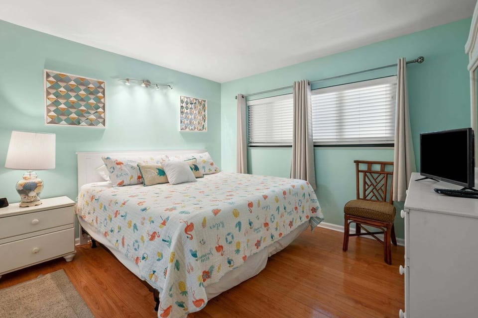 Bedroom with a patterned quilt, white nightstand and TV at Crescent Towers II 707 in Crescent Beach, North Myrtle Beach