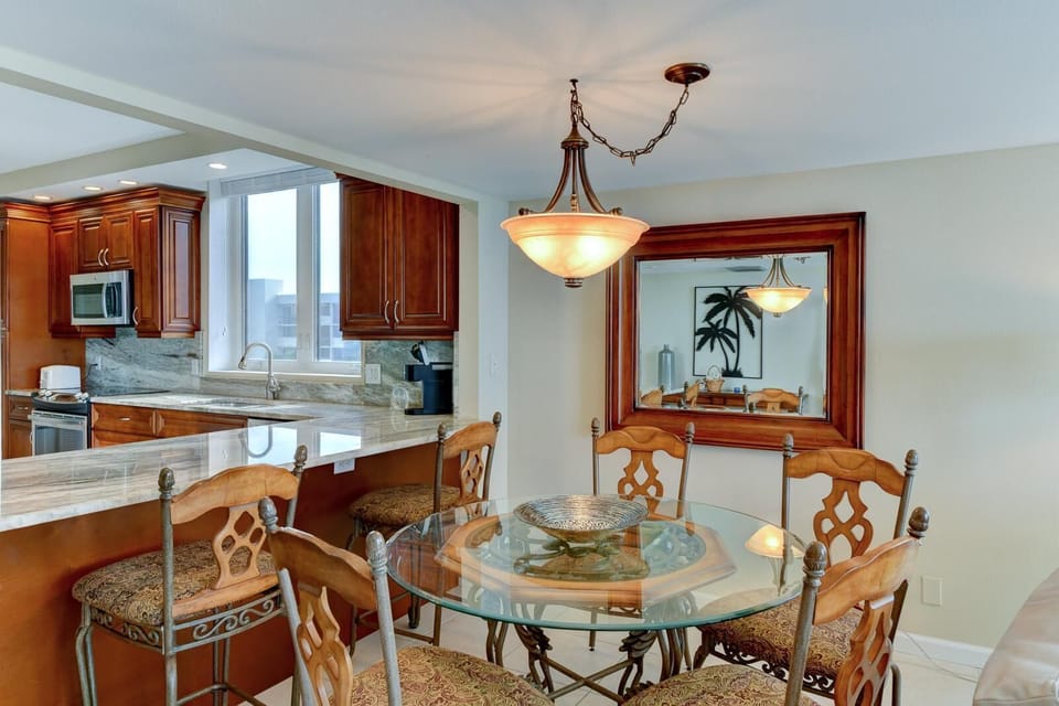 Kitchen counter with marble surface extends into bar seating with wrought iron and patterned cushions.