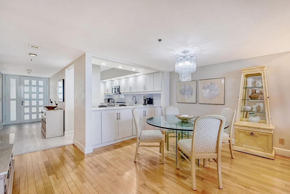 Light hardwood floors extend across the dining room, illuminated by a textured glass chandelier and soft wall art.