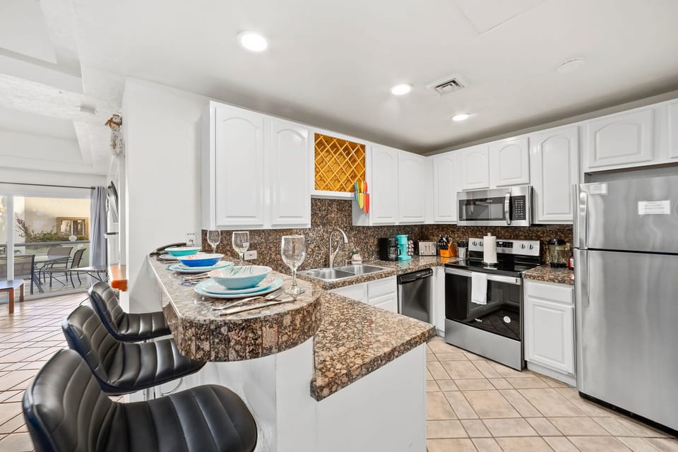 Fully equipped kitchen featuring granite countertops, stainless steel appliances, and bar seating for three.