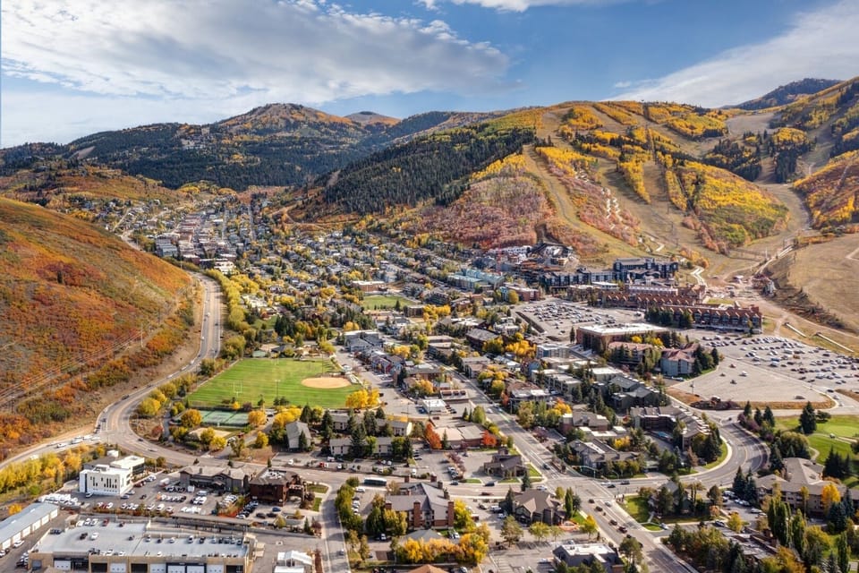 Mountain town nestled in colorful autumn foliage with ski slopes visible on surrounding peaks.