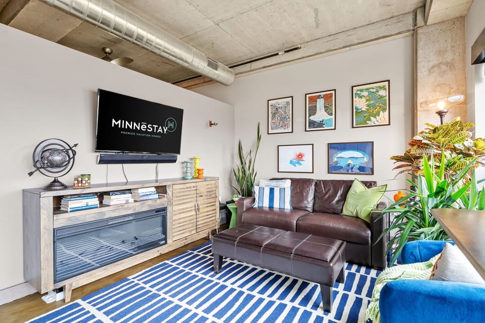Relax in your stylish living space with industrial charm, featuring a cozy leather sofa, vibrant artwork, and modern amenities.