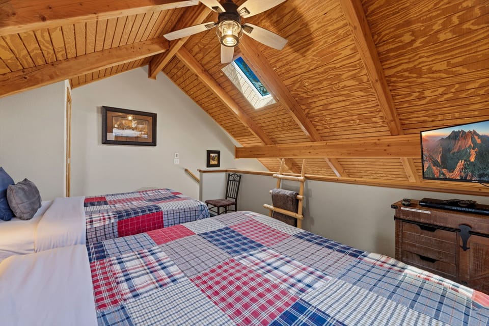 Drift off under soaring wood beams in this cozy loft bedroom with twin beds and natural light streaming through skylights above.