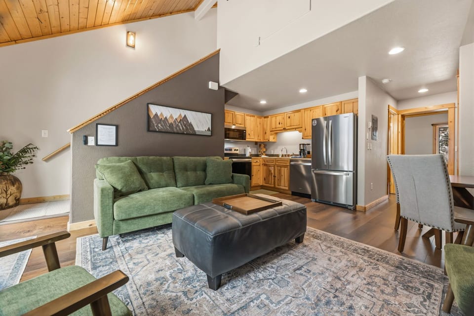 Sink into the plush green sofa beneath soaring wood ceilings, where mountain views and modern comfort meet in your open-concept retreat.