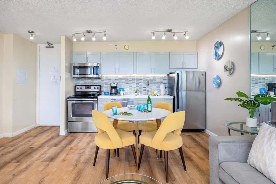 Modern kitchen and dining area with stainless steel appliances and yellow chairs.