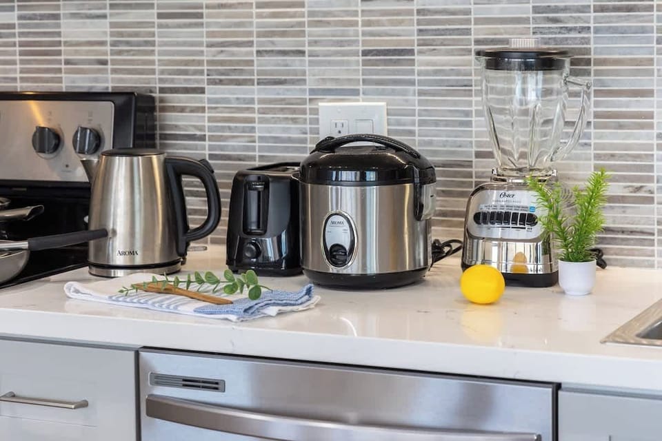 Modern kitchen countertop with essential appliances including a kettle, toaster, rice cooker, and blender.