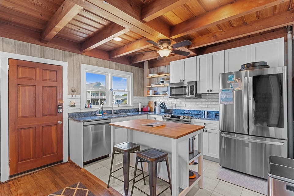 Kitchen with white cabinets, stainless appliances, blue countertops, open shelving, a butcher block island, and a warm wood beam ceiling.