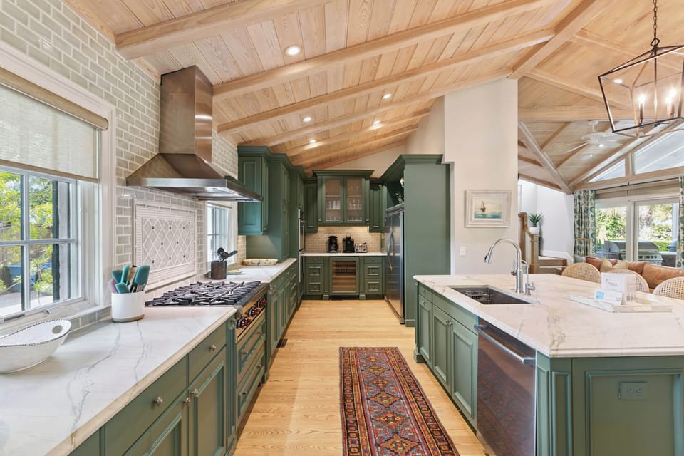 Picture yourself in this bright kitchen with vaulted wood ceilings, custom green cabinetry, and marble countertops—perfect for preparing meals or sipping morning coffee in style.
