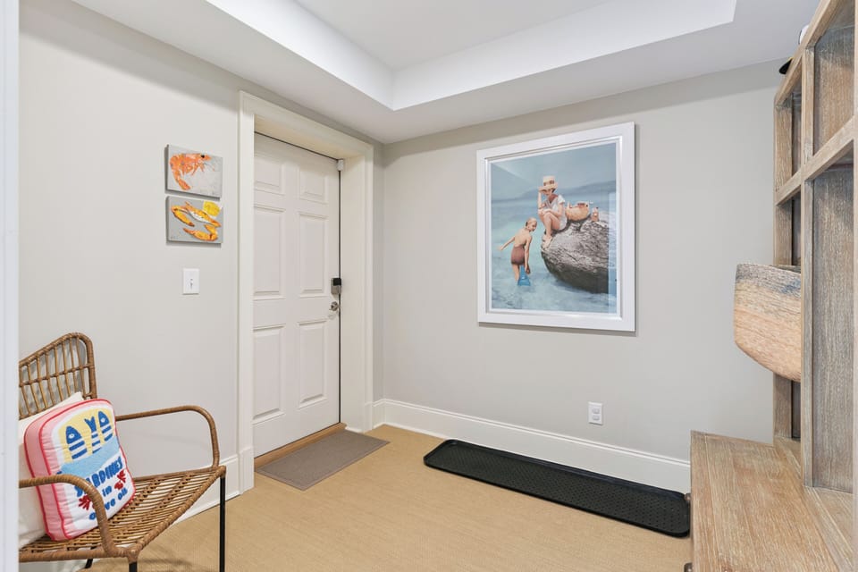 Step into your coastal retreat, where playful beach-themed art and a cozy wicker chair greet you, setting the tone for a relaxing seaside escape.