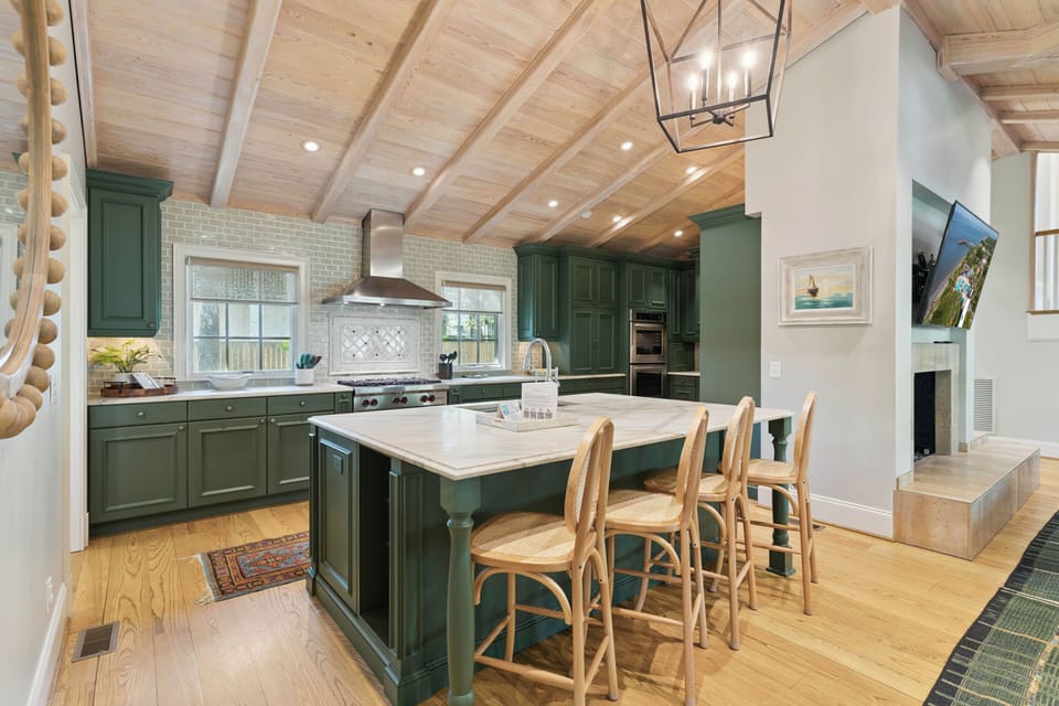 Step into your gourmet kitchen where vaulted wood ceilings and elegant green cabinetry create a cozy yet sophisticated cooking space. Gather at the spacious island for casual meals or coffee.