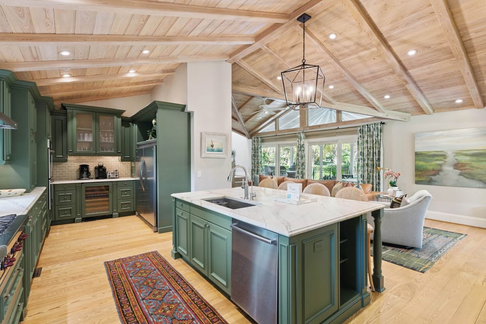 Gather in this open kitchen with rich green cabinetry, marble countertops, and soaring wood-beamed ceilings that invite warmth into every meal prep and conversation.