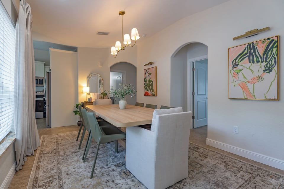 Gather around this elegant dining table where meaningful conversations unfold beneath soft chandelier lighting. The soothing palette and curated artwork create your perfect backdrop for memorable meals together.