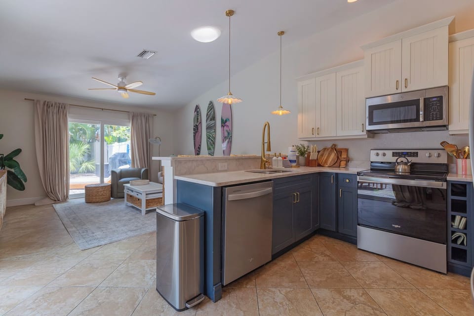 Step into your bright, beachy haven featuring a fully equipped kitchen with modern appliances, coastal pendant lighting, and an open flow into the living area where tropical décor sets the mood for relaxation.