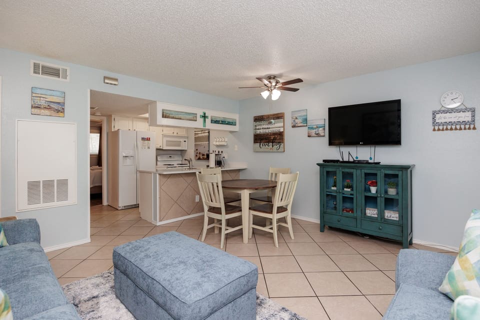Relax in your bright, coastal-themed living space featuring comfortable seating, beach artwork, and an open kitchen perfect for vacation meals.