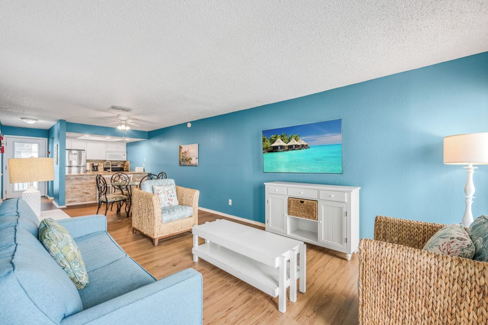 Relax in your bright coastal living room with tropical blue walls, wicker accents, and ocean artwork setting a beachy mood.