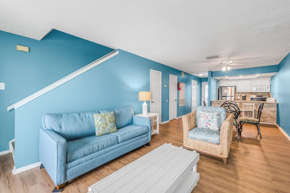 Relax in your spacious open-plan living area with coastal blue walls, comfortable seating, and a fully equipped kitchen.
