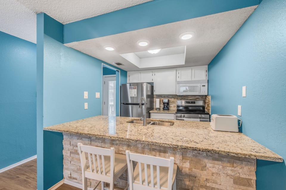Cook your favorite meals in this bright, fully-equipped kitchen featuring granite countertops, stainless steel appliances, and cheerful coastal blue walls.
