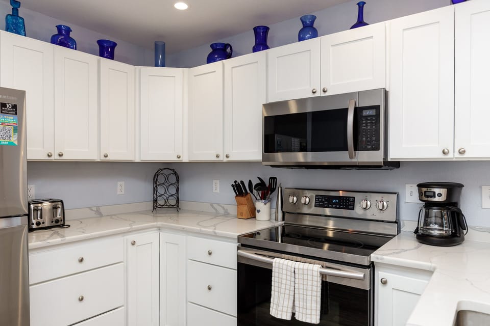 Your fully equipped kitchen invites home-cooked meals with stainless appliances, marble countertops, and thoughtful details like blue pottery creating warmth.