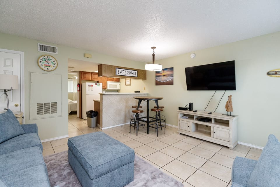 Your cozy living space features comfortable blue seating, a fully equipped kitchen, and entertainment center for perfect vacation relaxation.
