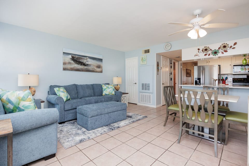 Relax in your bright open-concept living space with comfortable seating, coastal decor, and a convenient kitchen nearby for all your vacation needs.