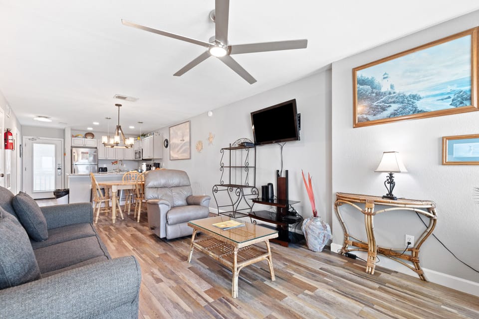Your open-concept living space combines comfort with coastal charm, featuring warm wood floors and seaside artwork that sets a relaxing vacation mood.