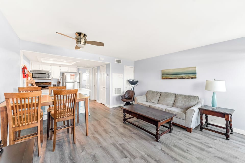 Relax in your bright, airy living space where modern comfort meets coastal charm, complete with ceiling fan and ocean artwork.