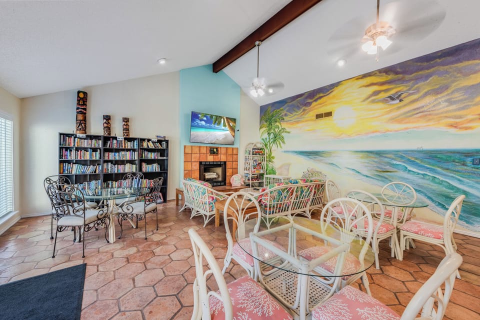 Relax in this vibrant communal space featuring comfortable seating, extensive book collection, and stunning ocean mural creating a peaceful beachside atmosphere.