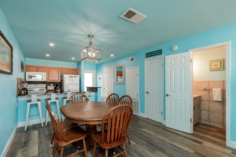 Your coastal-inspired kitchen and dining space features cheerful turquoise walls, a warm wood dining table for six, and glimpses into your private bathroom.