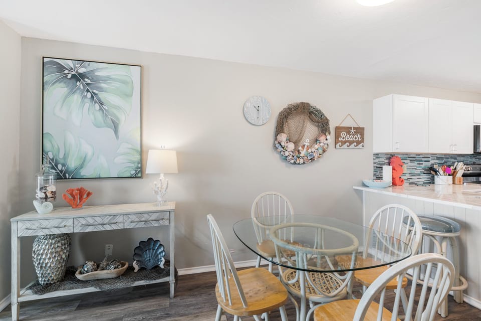 Your bright dining space features a glass table surrounded by coastal charm, where beach-inspired decor and soft lighting create perfect moments for shared meals.