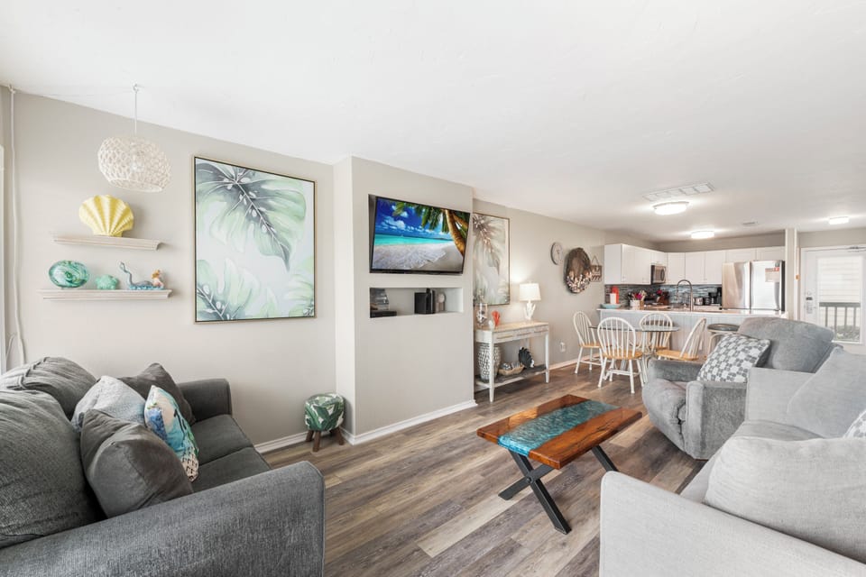 Relax in your thoughtfully designed living space featuring coastal artwork and comfortable seating that flows seamlessly into the fully equipped kitchen.