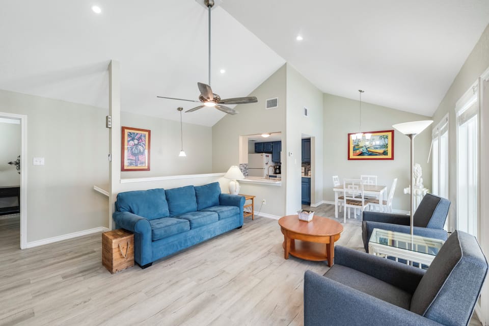 Relax in your spacious open-plan living area with vaulted ceilings, comfortable blue sofa, and coastal artwork creating a serene atmosphere.