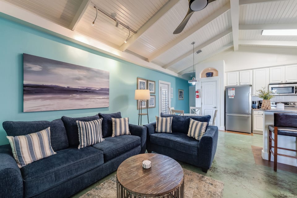 Sink into plush navy sofas beneath soaring white beams while you unwind in this bright, coastal-inspired living space.