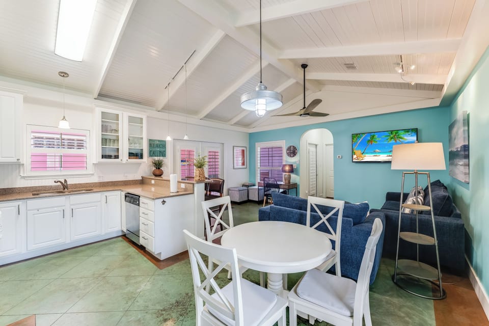 Your coastal retreat features open-plan living with turquoise walls, white kitchen, and tropical touches creating the perfect beach house atmosphere.