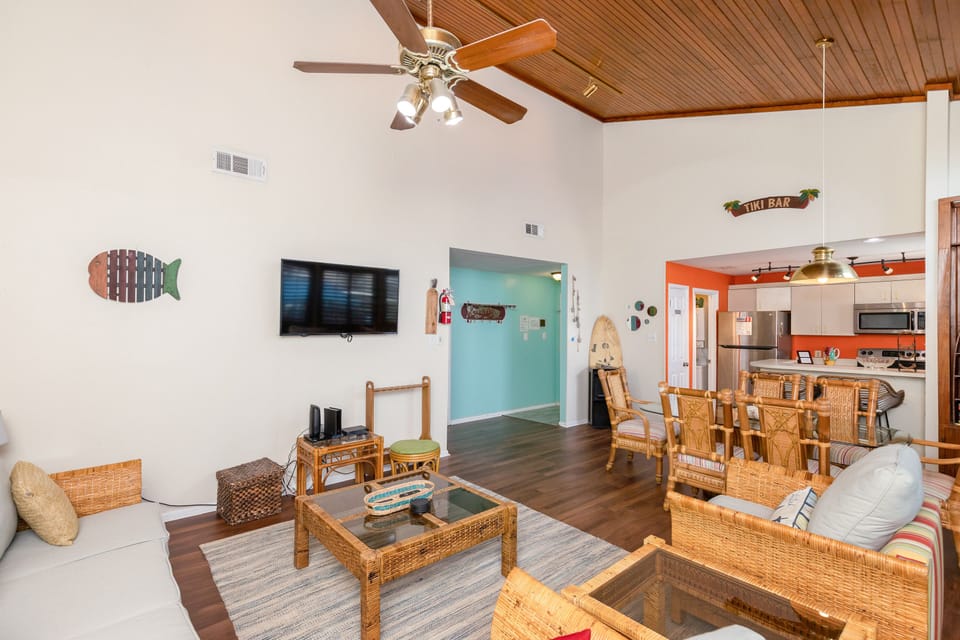Relax in your tropical-themed living space with wicker furniture, ceiling fans, and beach-inspired decor creating the perfect coastal retreat.