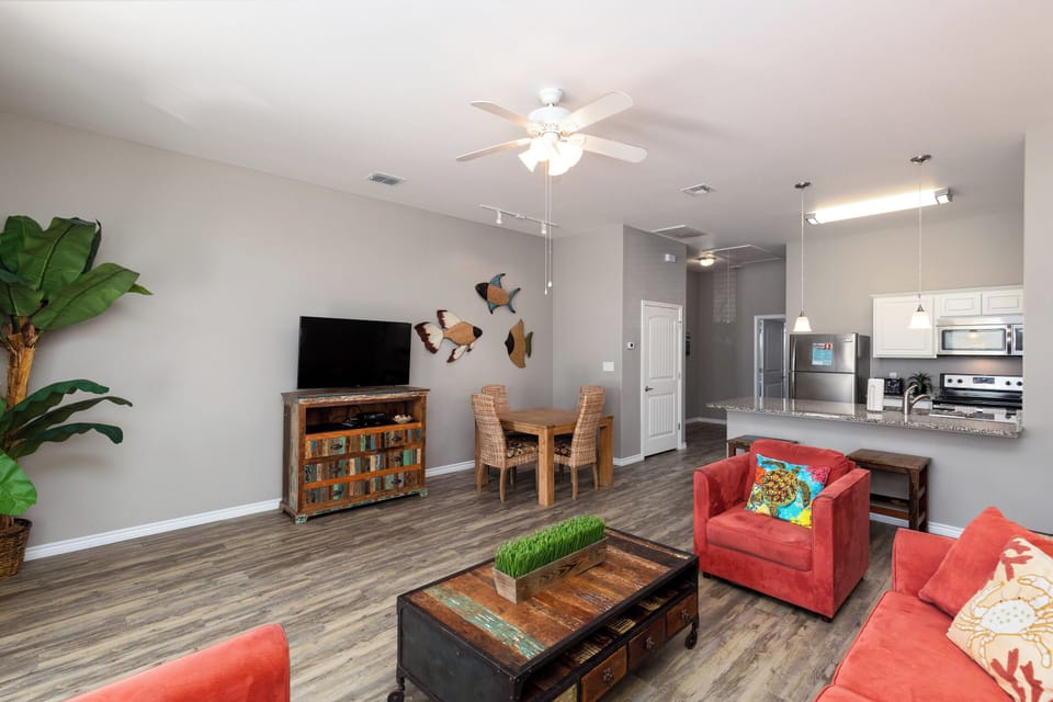 Relax in your spacious open-plan living area featuring vibrant coral seating, modern kitchen, and tropical touches that create a welcoming home away from home.