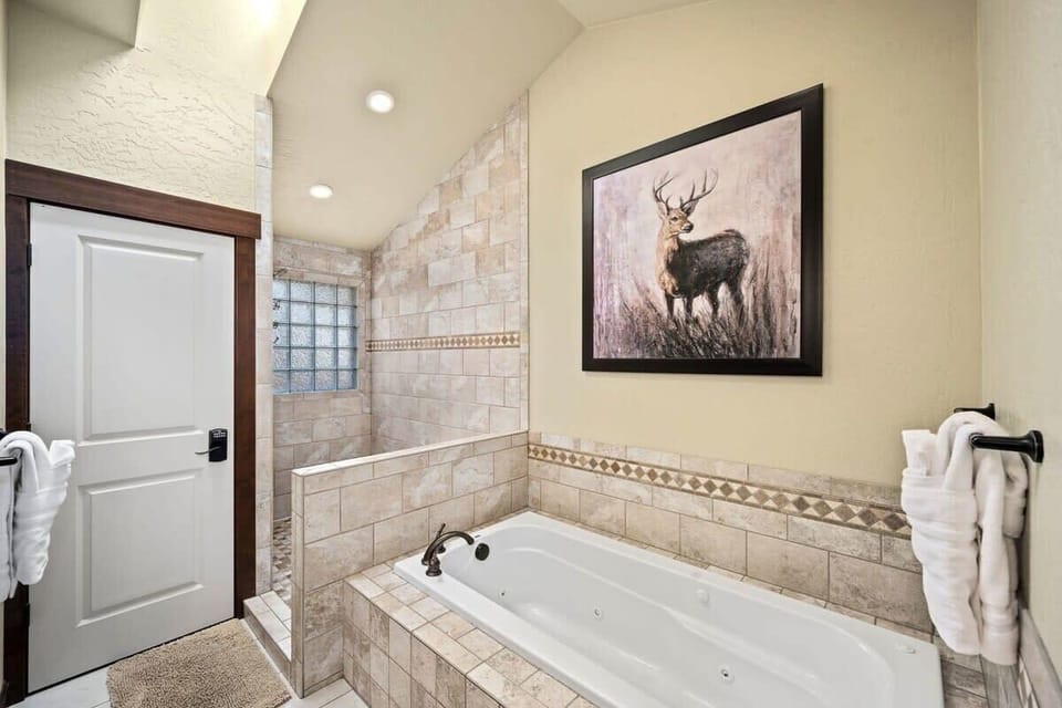 Unwind in your private spa-like bathroom with a deep soaking tub surrounded by elegant stone tile and charming rustic artwork.