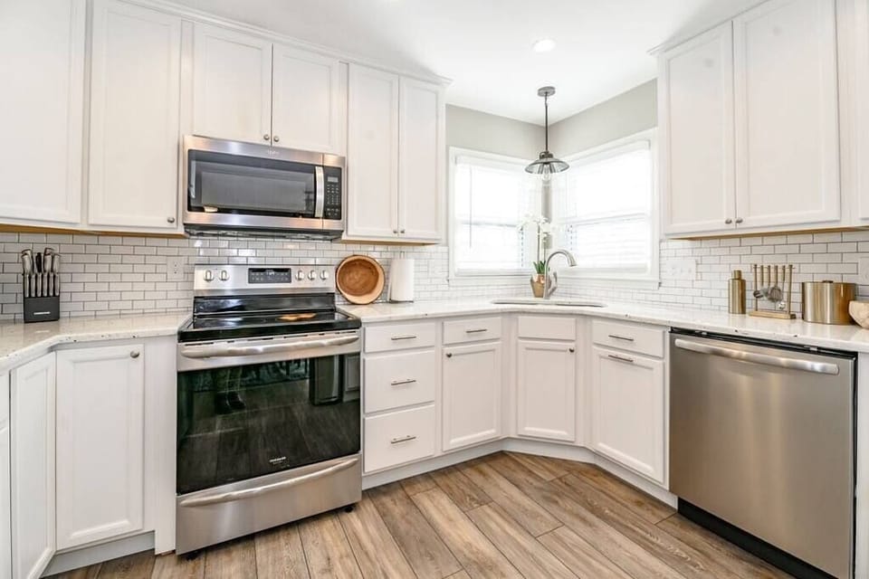 Modern kitchen featuring stainless steel appliances, including a refrigerator, oven, microwave, and dishwasher, paired with white cabinetry and quartz countertops for a clean, functional design.