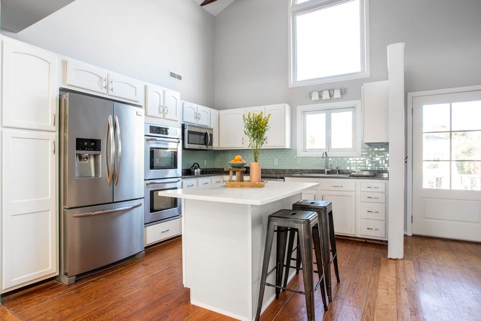 Modern, fully-equipped kitchen featuring white cabinetry, stainless steel appliances, and a central island with bar stool seating.