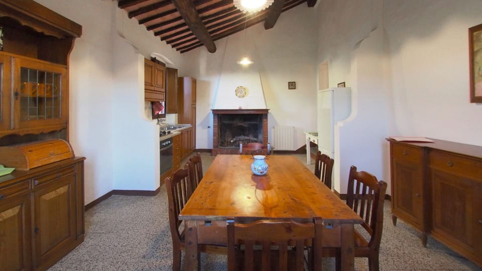 Spacious combination kitchen-dining room, full of light, with high beamed ceilings, windows on two sides, and large fireplace