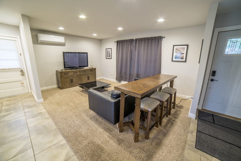 Living room with big screen TV, leather couch, and raised bar with seating for 3