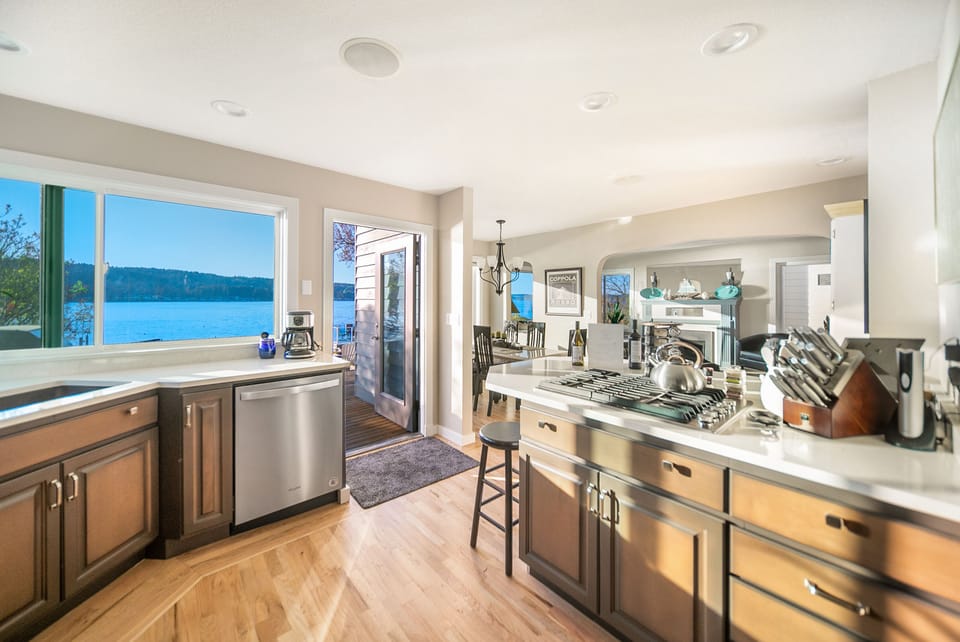 Bright kitchen with quartz counter tops, SS gas range, door leads out to deck. 