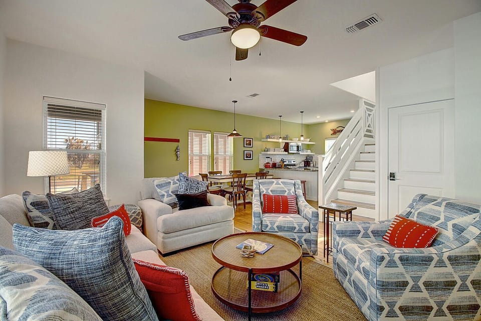 Unwind in your bright living room with cozy blue seating, colorful pillows, and an open layout connecting to the kitchen.