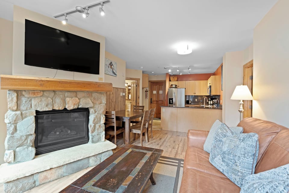 Your mountain retreat features an open-concept living space with a cozy stone fireplace, full kitchen, and warm lighting throughout—perfect for relaxing after adventure-filled days.