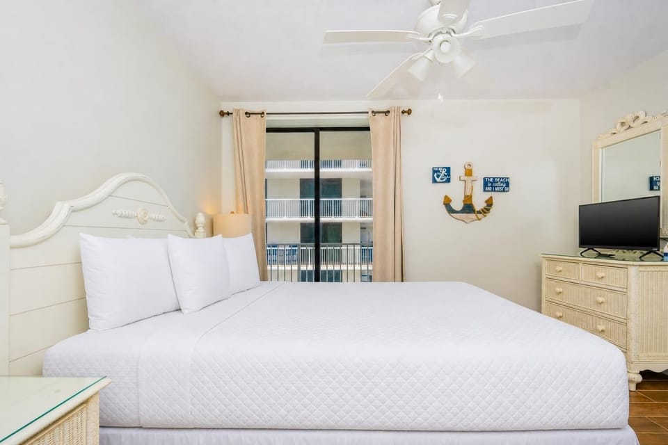 This inviting bedroom features a plush queen bed, light-colored decor, and a TV, creating a relaxing retreat
