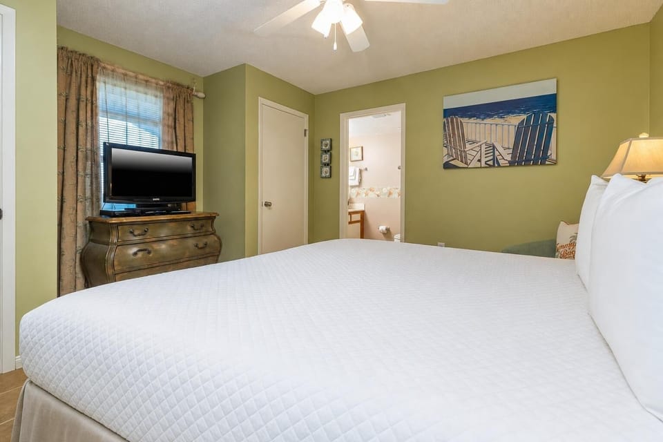Spacious guest bedroom features a comfortable king bed, a TV on a vintage dresser, and a vibrant beach artwork on the wall